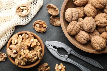 Fresh ripe walnuts, nutcracker and shells on black table, flat lay