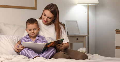 Mother with her little son reading story in bedroom at night