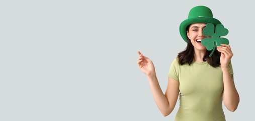 Happy young woman in leprechaun hat holding shamrock on grey background with space for text. St....