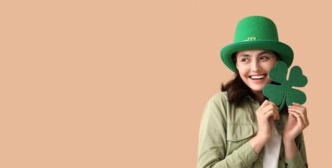 Happy young woman in leprechaun hat holding shamrock on beige background with space for text. St....