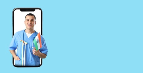Young male doctor with Indian flag looking out of smartphone screen on light blue background with...