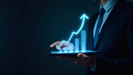 Businessman holding tablet and showing a growing virtual hologram of statistics, graph and chart with arrow up on dark background. Stock market. Business growth, Business background, Finance.