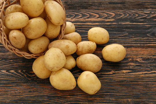 Wicker bowl with raw potatoes on wooden background