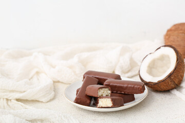 Plate with tasty chocolate covered coconut candies on light background