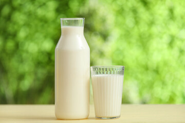 Glass and bottle of fresh milk on yellow wooden table outdoors