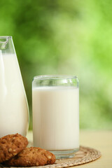 Glass and jug of fresh milk with sweet cookies on yellow wooden table outdoors