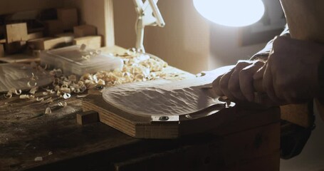 Luthier working on top plate of a violin using a gouge, with wood shavings on workbench and tools in background, crafting a musical masterpiece with precision and expertise, close up shot