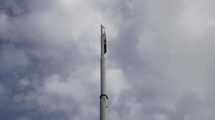 From a low angle view under a cloudy sky, a large Pakistani flag flies high on a towering pole.