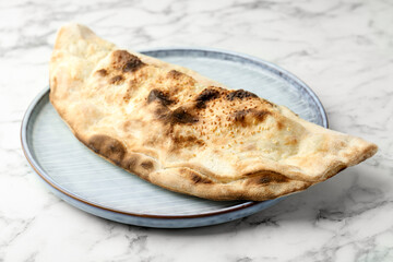Delicious calzone on white marble table, closeup