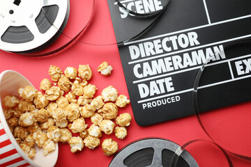 Movie clapper, sweet popcorn and film reels on red background, flat lay