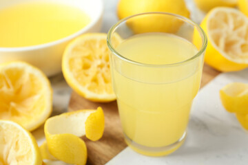 Glass of fresh lemon juice and squeezed fruits on table, closeup