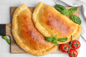 Tasty vegetarian calzones with basil and tomatoes on white tiled table, top view