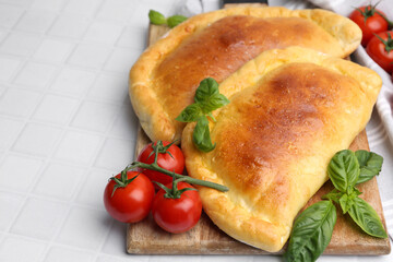 Tasty vegetarian calzones with basil and tomatoes on white tiled table, closeup. Space for text