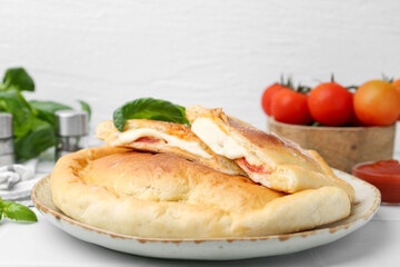 Pieces of delicious calzone pizza with mozzarella, tomatoes and basil on white table, closeup