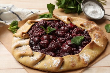 Tasty galette with cherries, mint and powdered sugar on wooden table, closeup