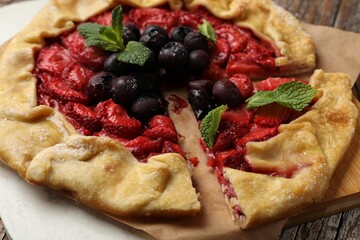Tasty galette with strawberries, blueberries and mint on table, closeup