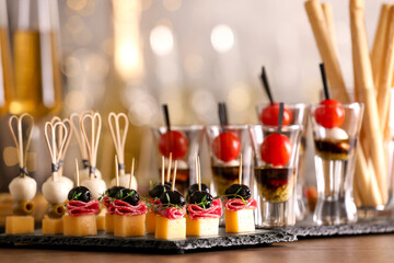 Many different tasty canapes on wooden table against blurred lights, closeup