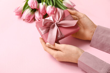 Female hands with gift box and tulips on pink background