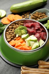 Natural and dry pet food in feeding bowl among products on dark textured table, closeup