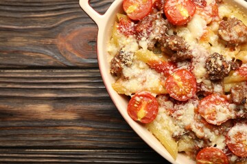 Delicious pasta casserole with cheese, tomatoes and minced meat in baking dish on wooden table, top view. Space for text