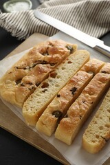 Slices of delicious focaccia bread with olives, thyme, salt and knife on black table, closeup