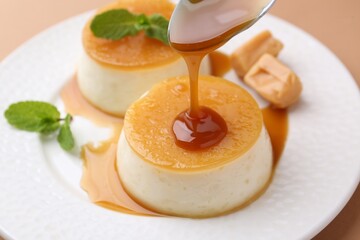Pouring caramel sauce onto tasty pudding on light brown background, closeup