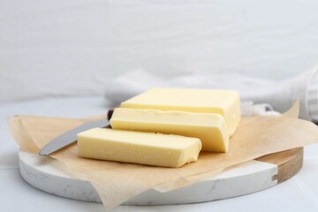 Cut block of fresh butter and knife on white table, closeup