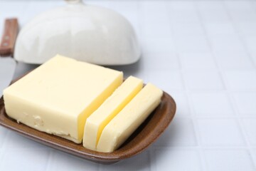 Cut tasty butter in dish on white tiled table, closeup. Space for text