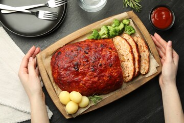 Woman serving delicious turkey meatloaf at black table, top view