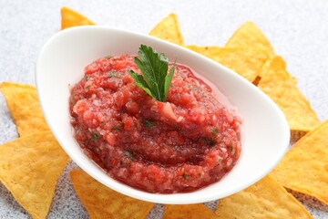 Spicy salsa sauce in gravy boat and nachos on light grey table, closeup