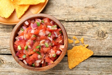 Delicious salsa in bowl and nacho chips on wooden table, flat lay
