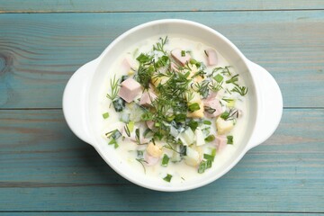 Delicious okroshka soup in bowl on light blue wooden table, top view