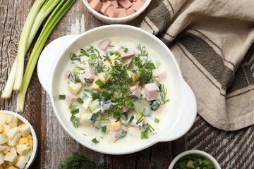 Delicious okroshka soup in bowl and ingredients on wooden table, flat lay