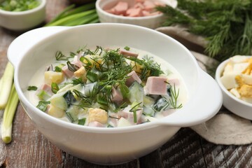 Delicious okroshka soup in bowl and ingredients on wooden table, closeup