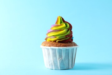 One delicious cupcake with colorful cream on light blue background, closeup
