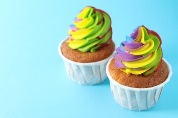 Delicious cupcakes with colorful cream on light blue background, closeup. Space for text