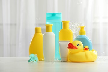 Baby cosmetic products, pacifier, rubber ducks and flying bubbles on light wooden table indoors