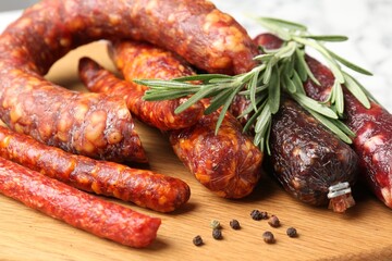 Different smoked sausages, rosemary and peppercorns on wooden board, closeup