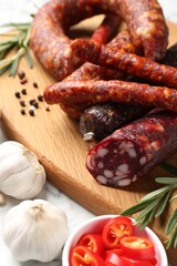 Different smoked sausages, chili pepper and garlic on white table, closeup