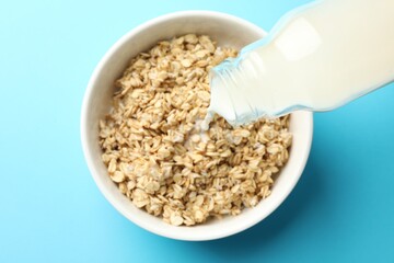 Pouring milk into bowl with oatmeal at light blue table, top view