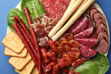 Different smoked sausages and other snacks on blue background, top view