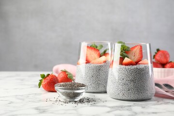 Delicious chia pudding with strawberries and mint in glasses on white marble table, space for text