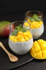 Delicious chia pudding with mango and mint in glasses on dark table, closeup