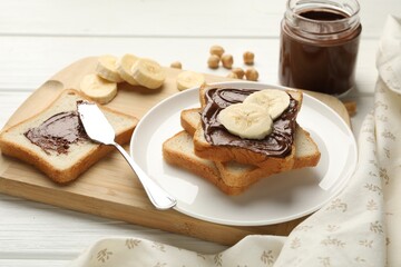 Sandwiches with chocolate butter, bananas and hazelnuts on white wooden table, closeup