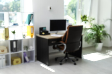 Interior of office with workplace, armchair, modern computer and shelving unit, blurred view