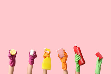 Female hands in rubber gloves holding bottles of detergent, jar with cleaning agent and sponges on pink background
