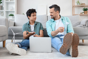 Teenage boy and his father with wind turbine models using laptop at home