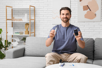 Diabetic young man with lancet pen and glucometer sitting on sofa at home