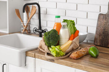 Shopping bag with different fresh products near sink on counter in kitchen