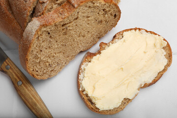 Fresh bread with butter and knife on white tiled table, top view